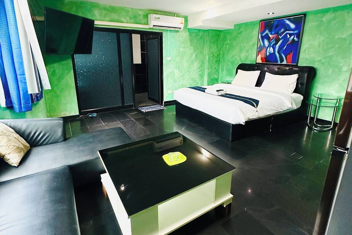 A modern hotel room with a bed, a sofa, a coffee table, and a painting on the wall.