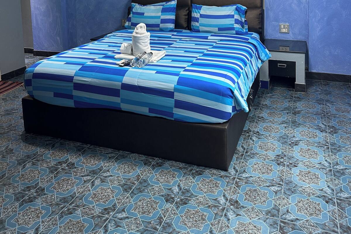 A modern bedroom with a large bed, a headboard, a nightstand, and a painting on the wall.