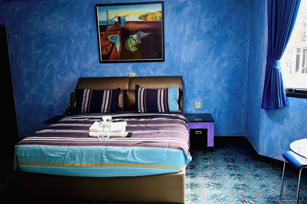 Une chambre avec un grand lit, une table de chevet, une chaise et un tableau au mur.