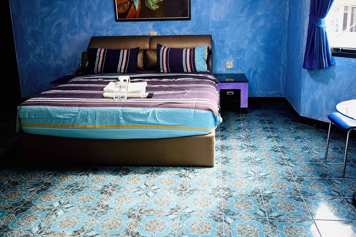A bedroom with a large bed, a nightstand, a chair, and a painting on the wall.