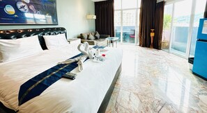 Une chambre d’hôtel avec un lit bien fait, un canapé, une petite table et une vue sur l’extérieur grâce à de grandes fenêtres.