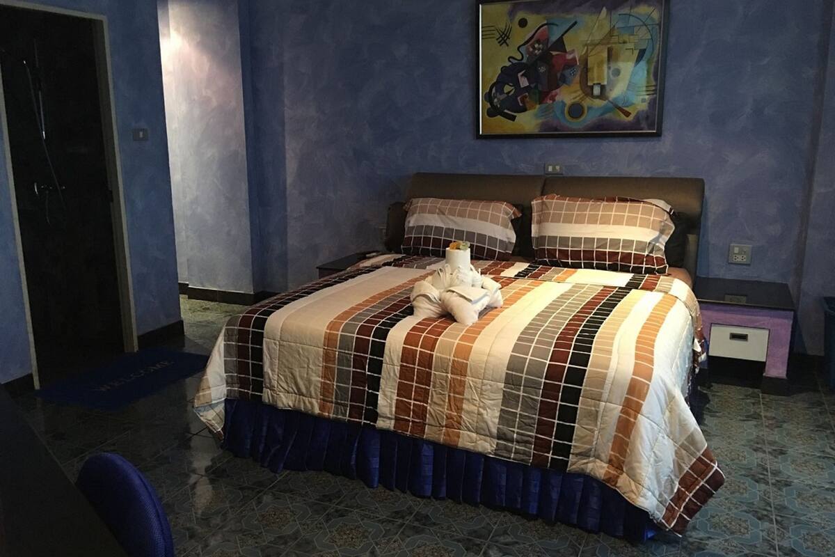 A hotel room with a large bed, a painting on the wall, and a nightstand with a lamp.