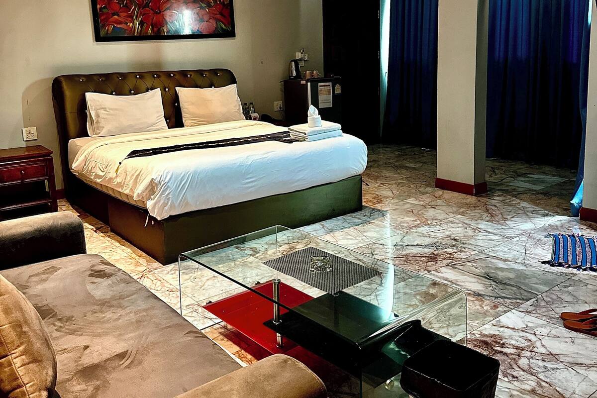 A modern hotel room with a large bed, a glass coffee table, a sofa, and a painting on the wall.