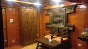 A room with a wooden wardrobe, a wooden chair with a cushion, a small table with a tissue box, and a decorative wall panel. - Temple House (Lalitpur)