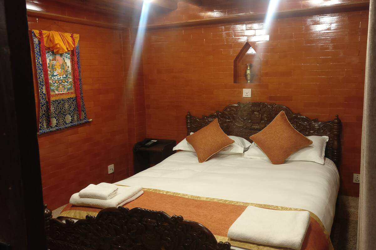 A hotel room with a wooden headboard, a bed with two pillows, a folded towel, and a small nightstand with a lamp.