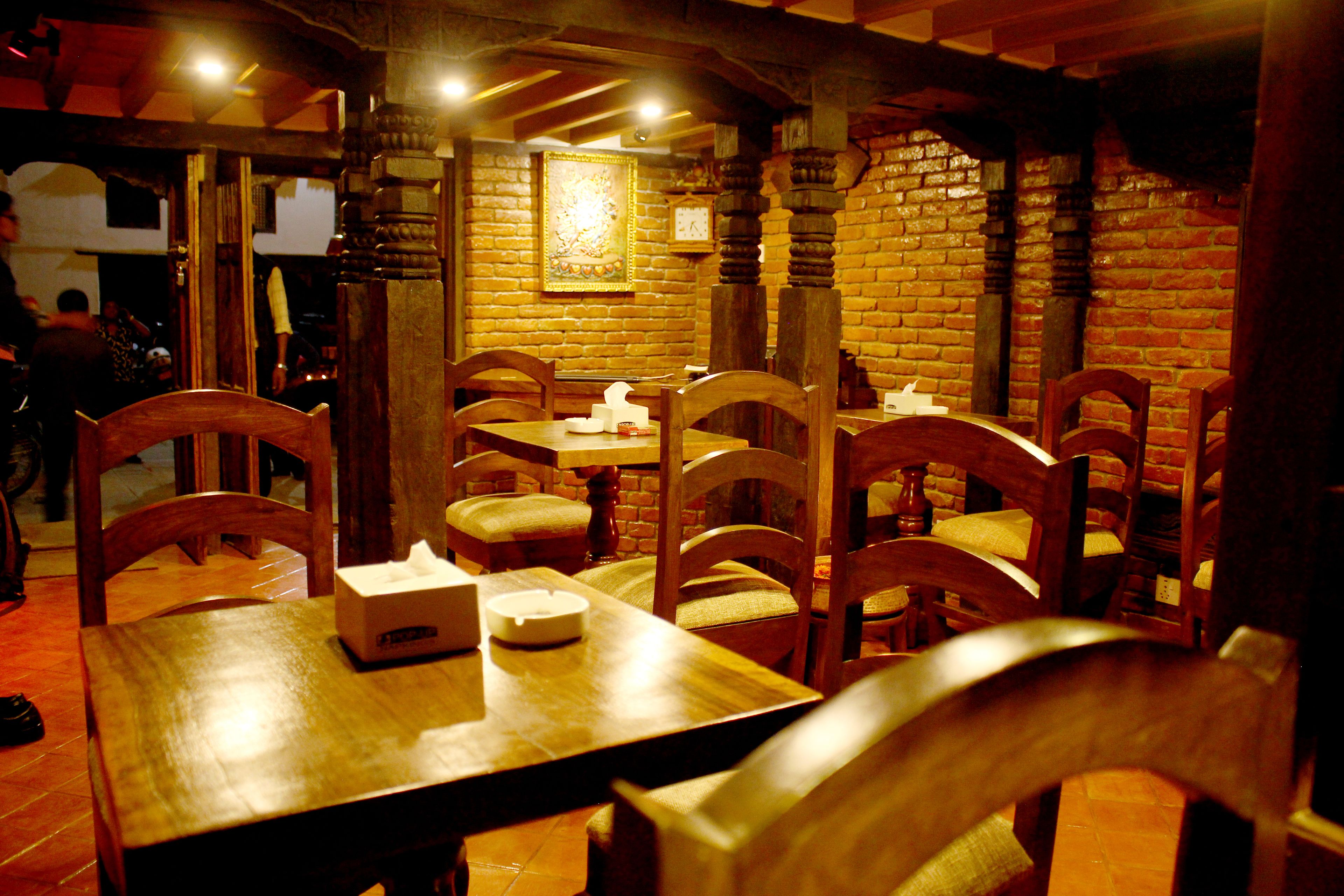 Un interior de restaurante con mesas y sillas de madera, paredes de ladrillo y un reloj en la pared.