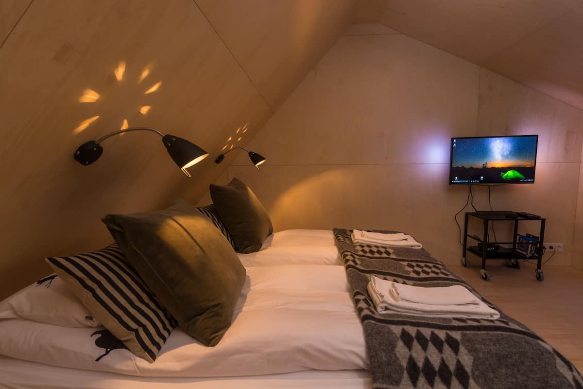 A cozy room with a bed, pillows, a blanket, a TV, and a cart with items.