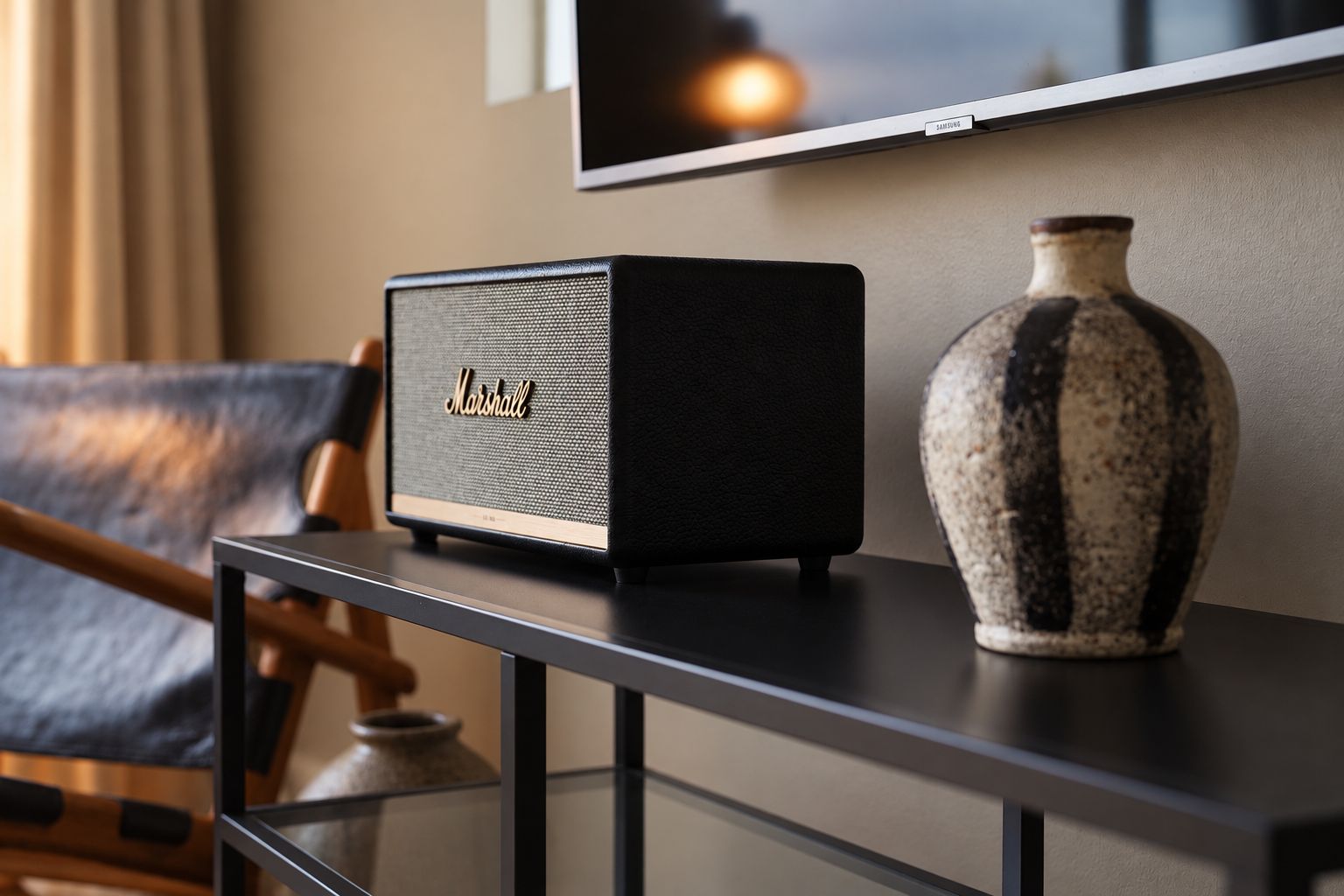 A black Marshall speaker on a black table with a vase and a chair in the background.