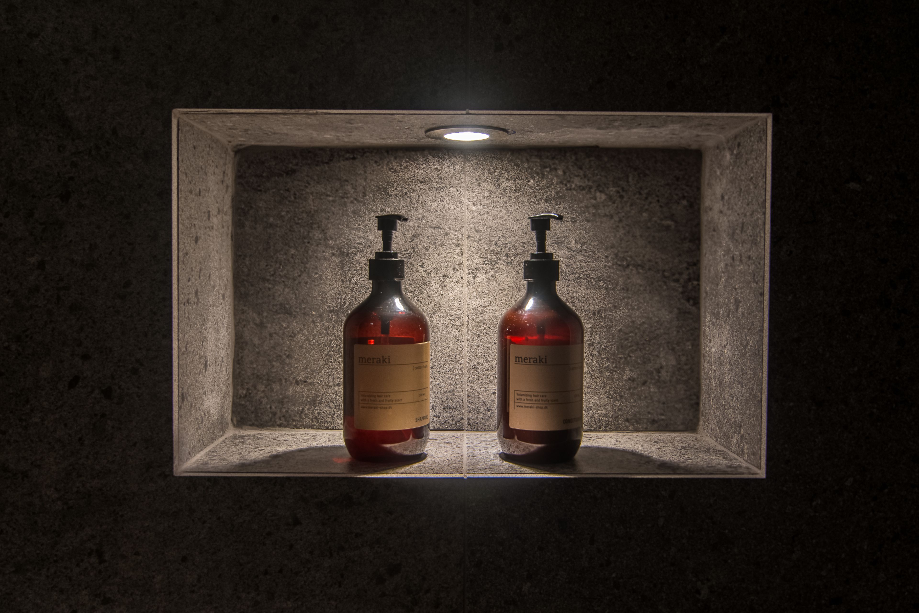 Dos botellas de Meraki en un hueco empotrado con pared texturizada y una lámpara en el techo.