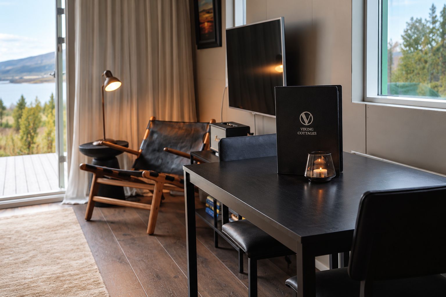 A modern room with a wooden table, a leather chair, a TV, and a window with a view of the outdoors.