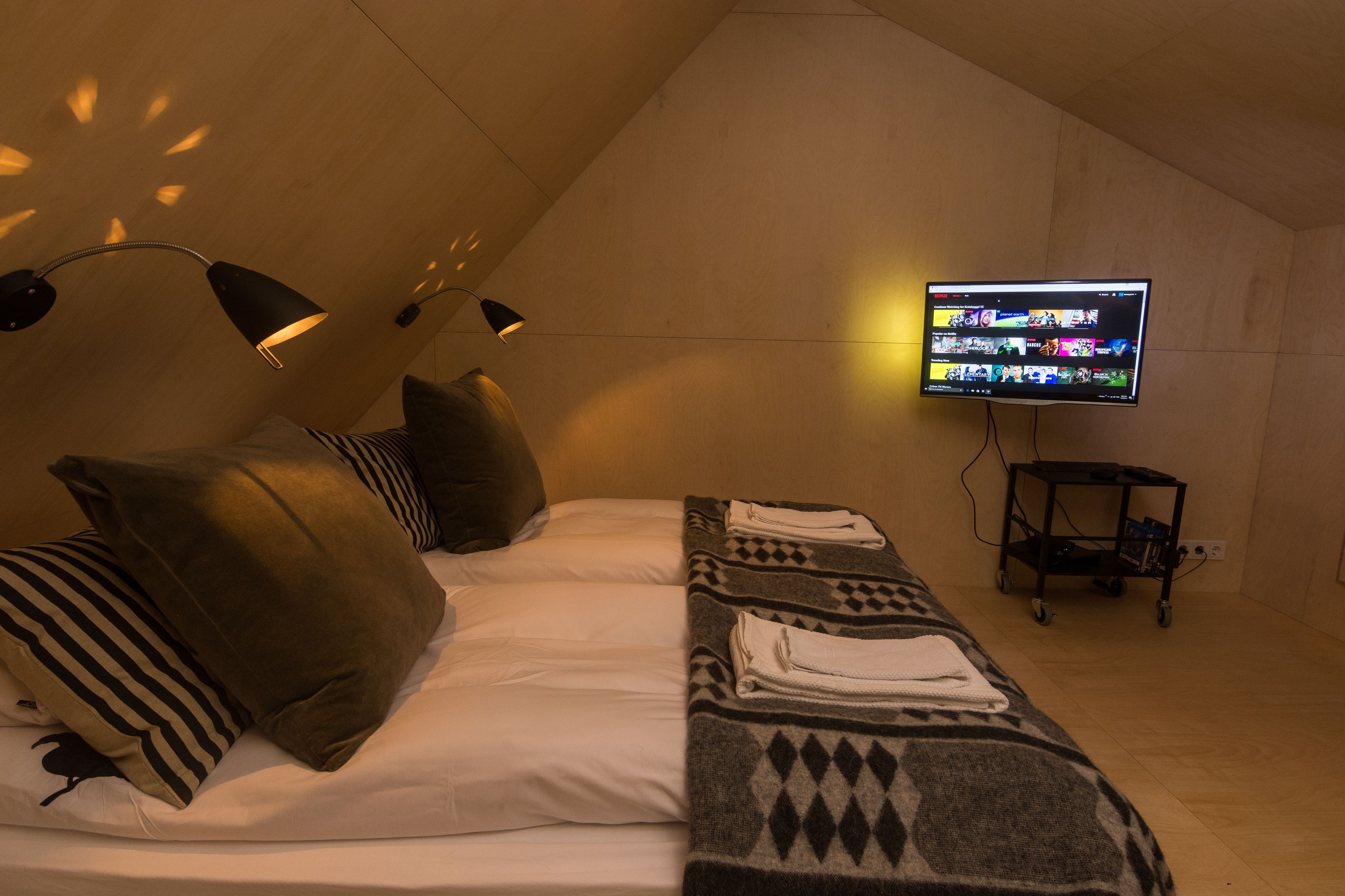 A bedroom with a bed, pillows, a blanket, a TV, and a desk with a chair.