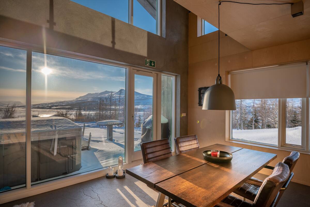 A modern dining area with large windows, a wooden table, and leather chairs.