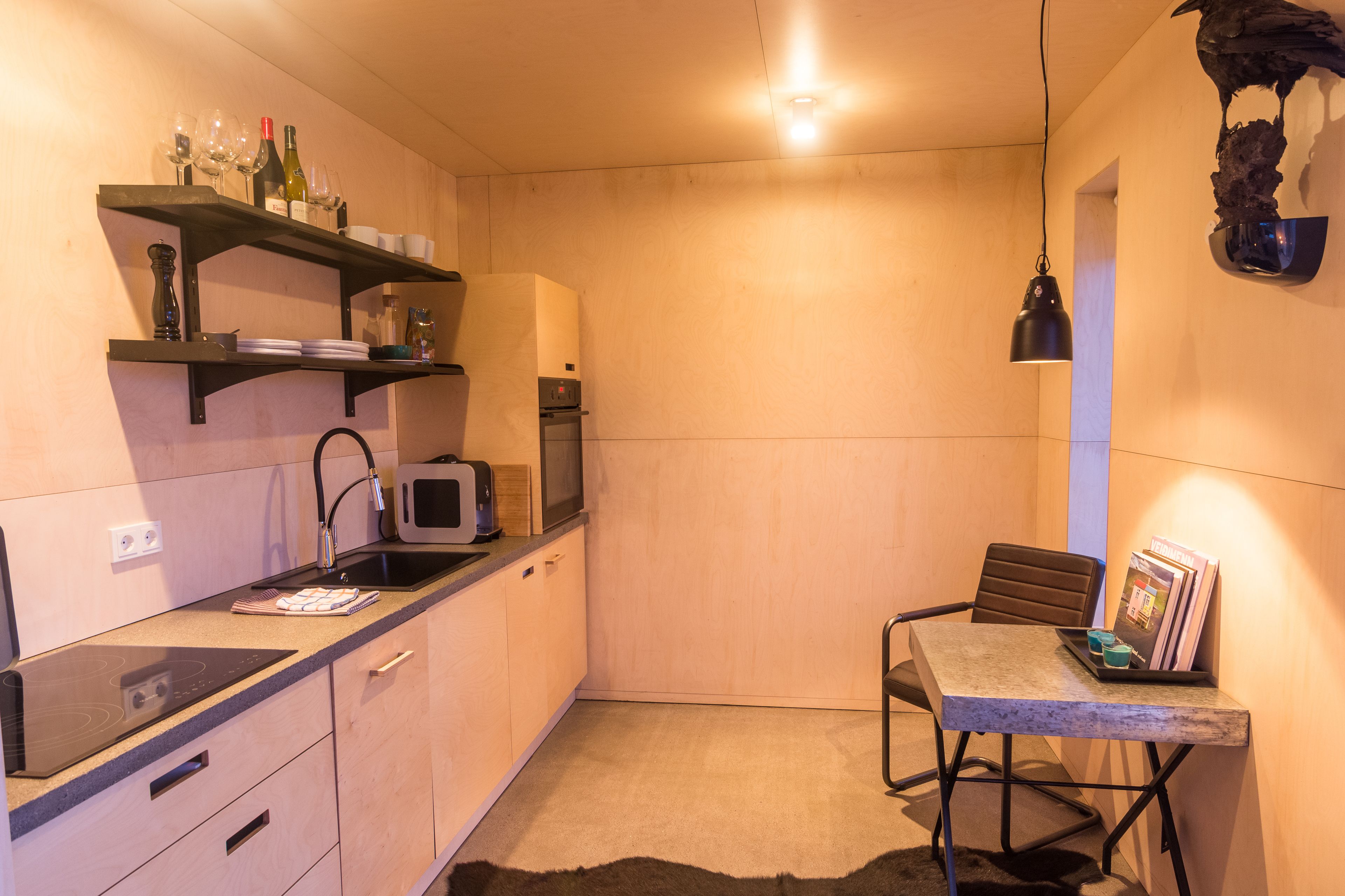 A compact kitchen with a microwave, toaster, and wine bottles on shelves.