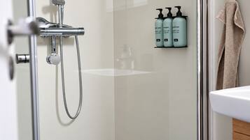 A modern bathroom with a glass shower enclosure, a white sink, and a towel rack with a beige towel.