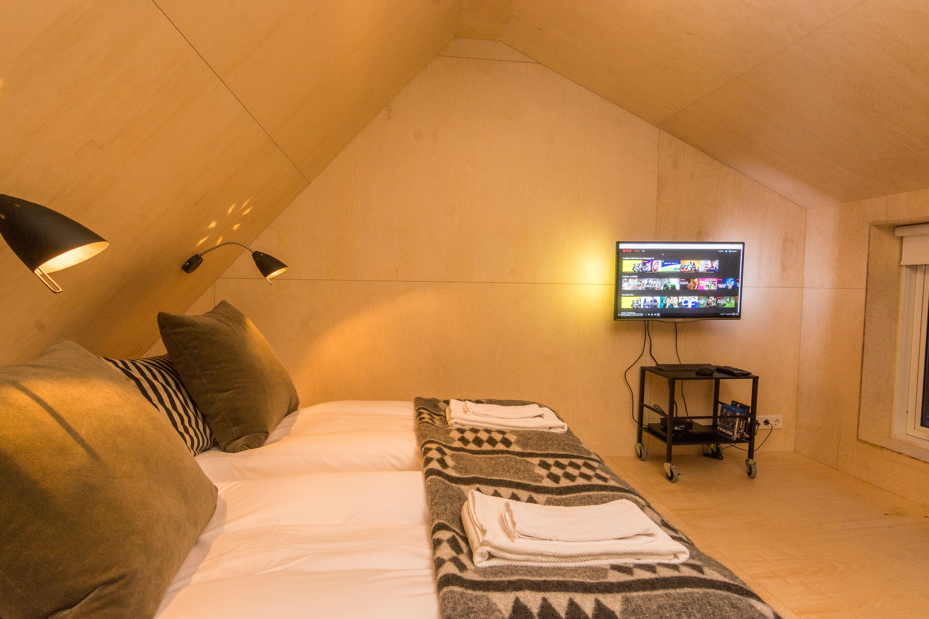 A cozy room with a bed, a flat-screen TV mounted on the wall, and a small cart with books and a remote.