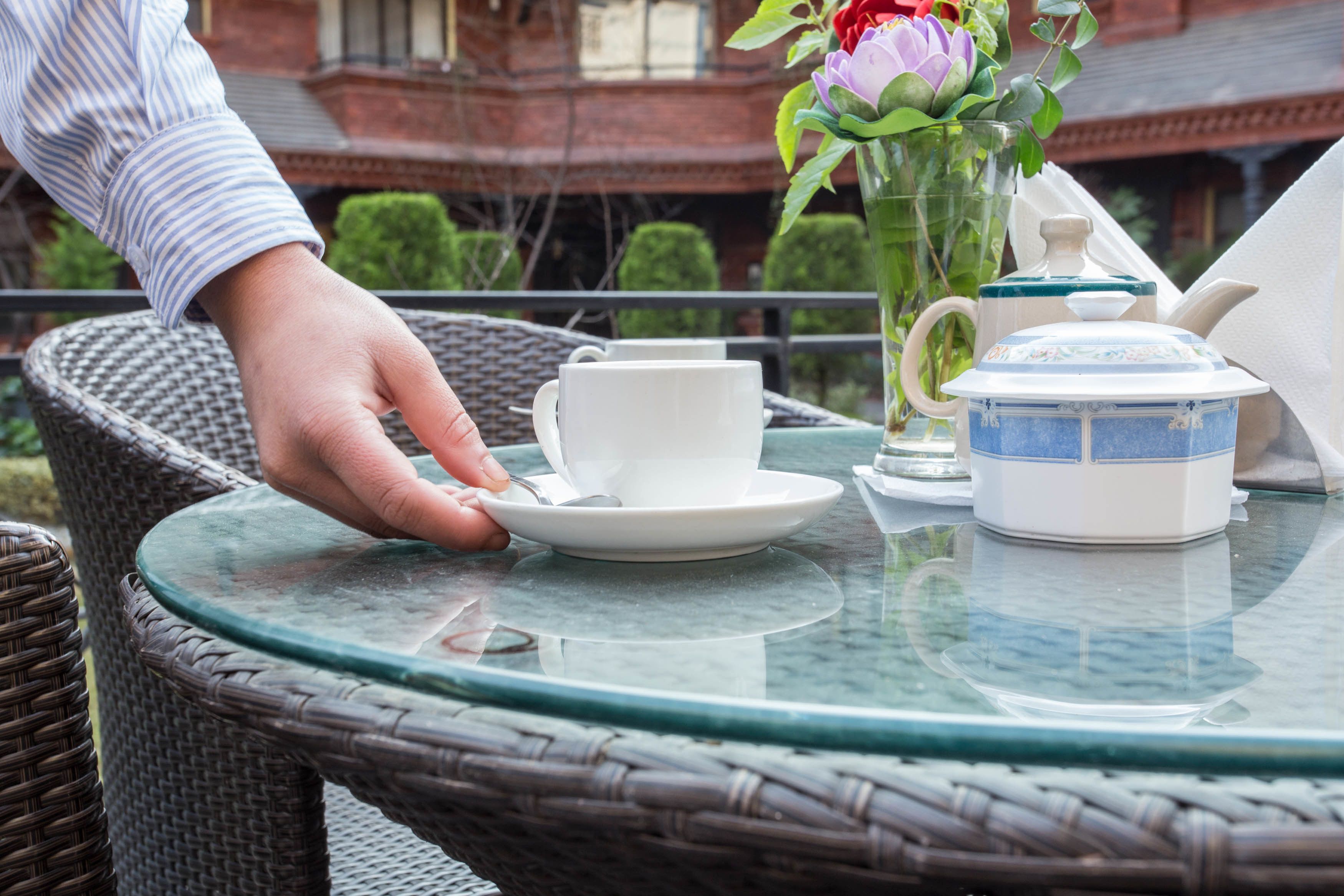 A wicker chair with a glass table, a white teapot, a white cup, and a white saucer.
