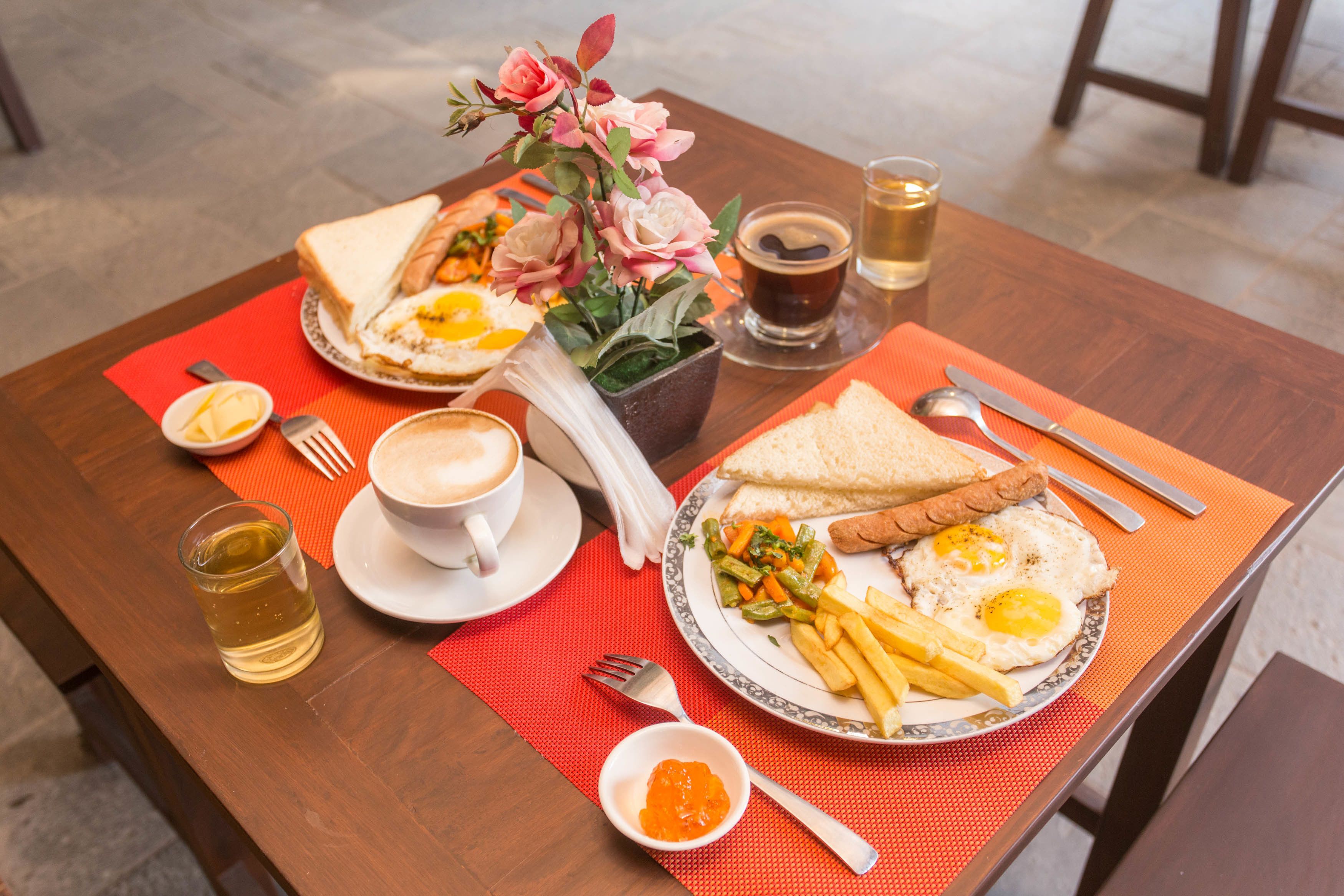 A table set with breakfast including eggs, toast, and fries, along with a cup of coffee and a glass of tea.