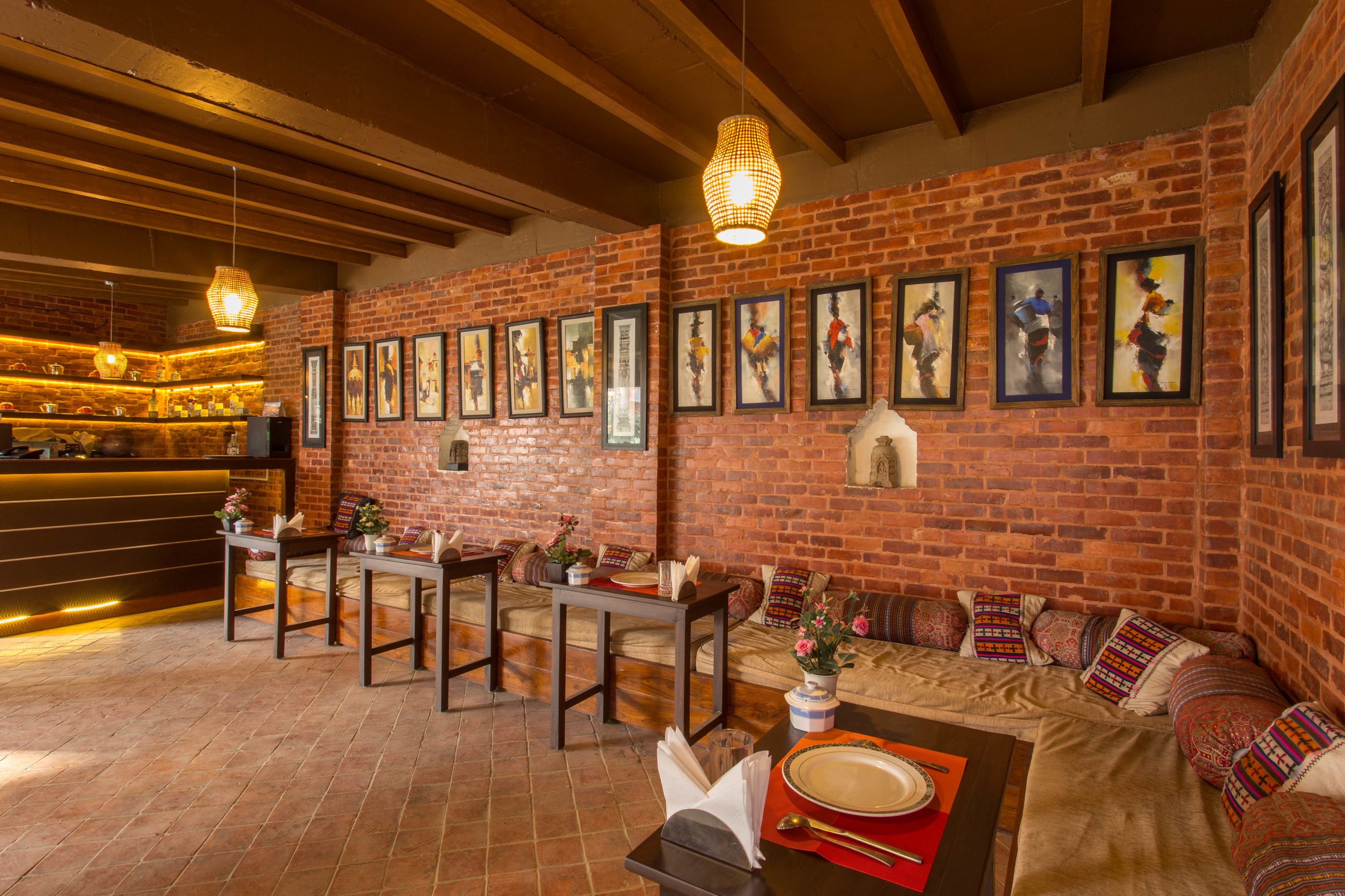 A restaurant with brick walls, wooden beams, and a bar area. There are tables and chairs, and artwork on the walls.