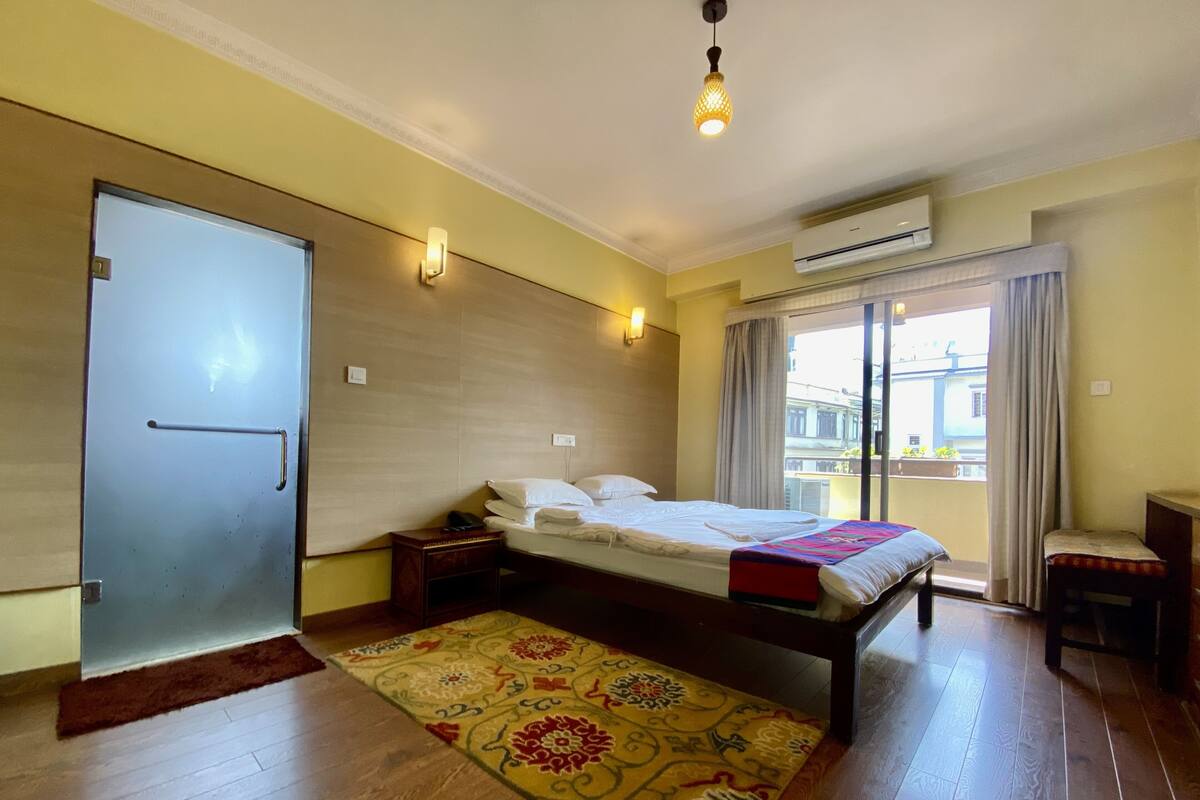 A hotel room with a bed, bedside table, nightstand, and a window with curtains.