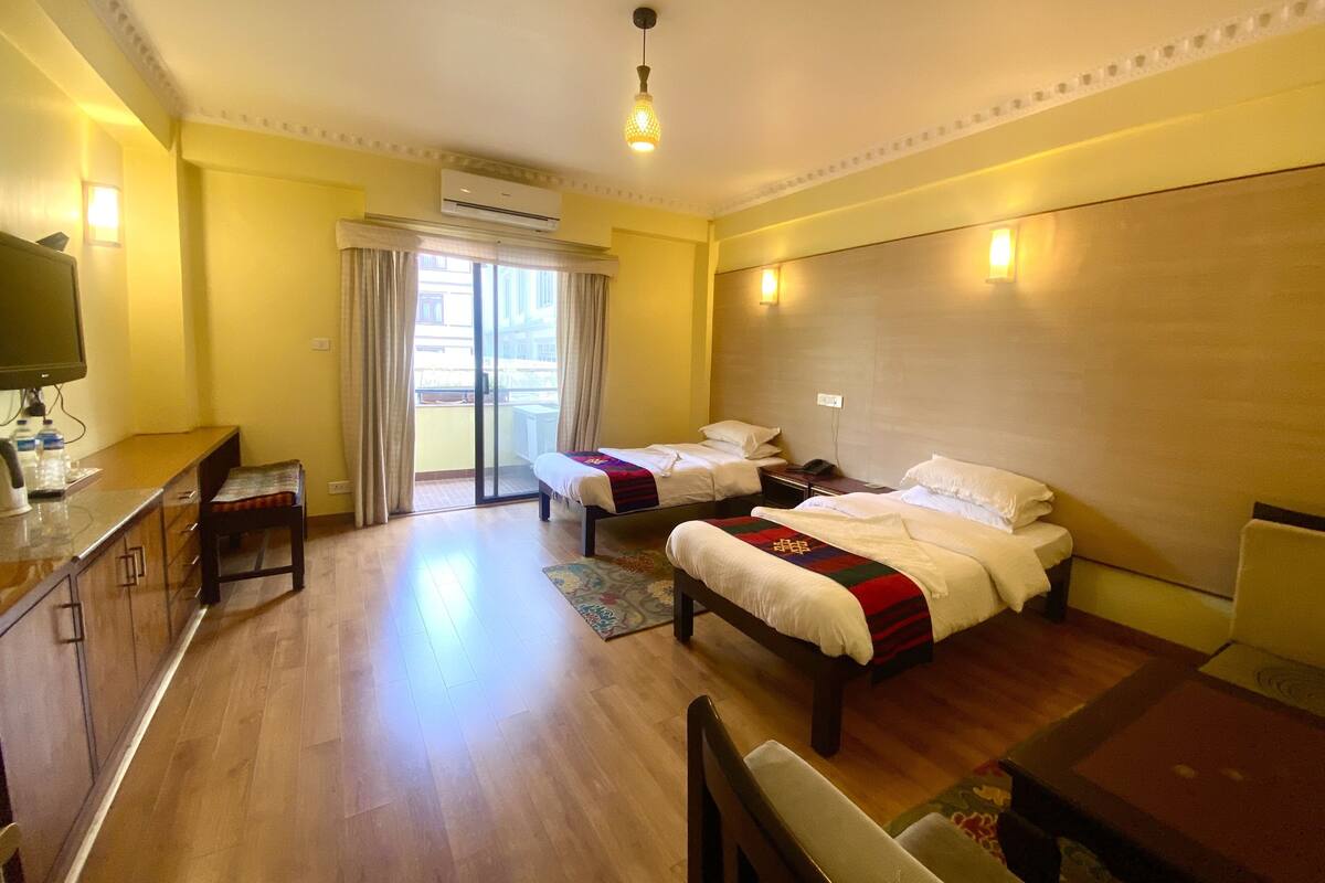 A hotel room with two beds, a desk with a chair, a television, and an air conditioning unit.