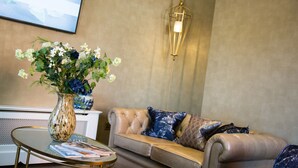 A living room with a beige sofa, a glass coffee table, and a vase with flowers. - Arden House (Stratford-upon-Avon)
