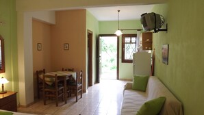 A dining area with a table and chairs, a sofa, and a refrigerator. - Pefka Studios & Apartments (Sithonia)