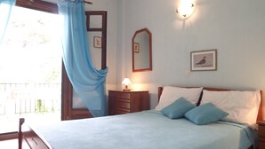 A bedroom with a bed, a nightstand, a lamp, a mirror, and a window with curtains. - Pefka Studios & Apartments (Sithonia)
