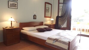 Una cama bien hecha con almohadas y colcha, dos lámparas de noche, una mesita de madera, un cajón pequeño y un cuadro colgado en la pared.