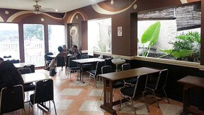 A restaurant with a checkered floor, tables, and chairs. There are large windows with plants and a view outside. - Hotel Fiducia Otista 153 (Jakarta)