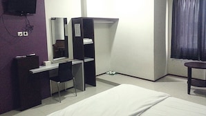 A hotel room with a bed, a desk with a chair, a wardrobe, a television mounted on the wall, and a window with curtains. - Hotel Fiducia Otista 153 (Jakarta)