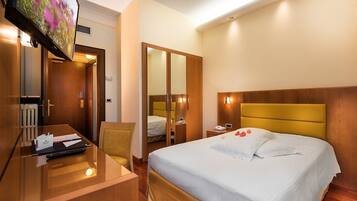 Een hotelkamer met een bed, nachtkastje, bureau, stoel en een aan de muur bevestigde televisie.