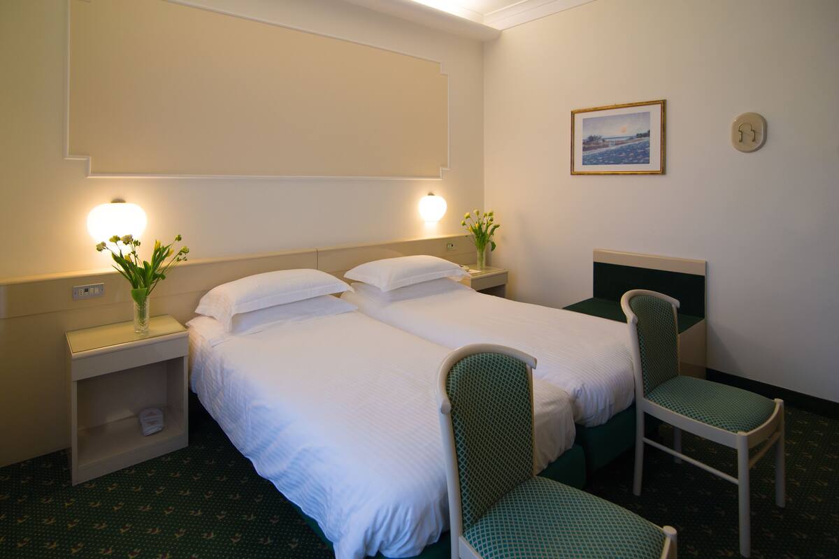 Een hotelkamer met twee bedden, een stoel, een nachtkastje en een aan de muur hangend schilderij.