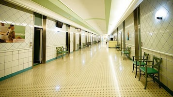 A hotel corridor with a tiled floor, green chairs, and a reception desk.