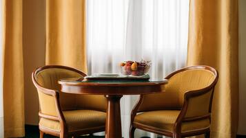 Um quarto com uma mesa de madeira redonda, duas cadeiras amarelas acolchoadas e uma tigela de frutas sobre a mesa.