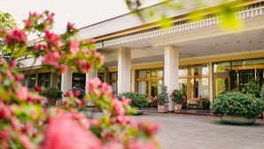 Entrada de hotel com área externa coberta, colunas e plantas em vasos.