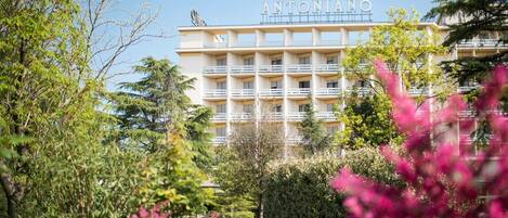 Et hotel med flere etager, der hedder ANTONIANO, med altaner og en have i forgrunden.