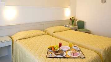 A hotel room with two beds, a bedside table with a phone and a vase of flowers, and a tray with breakfast items.