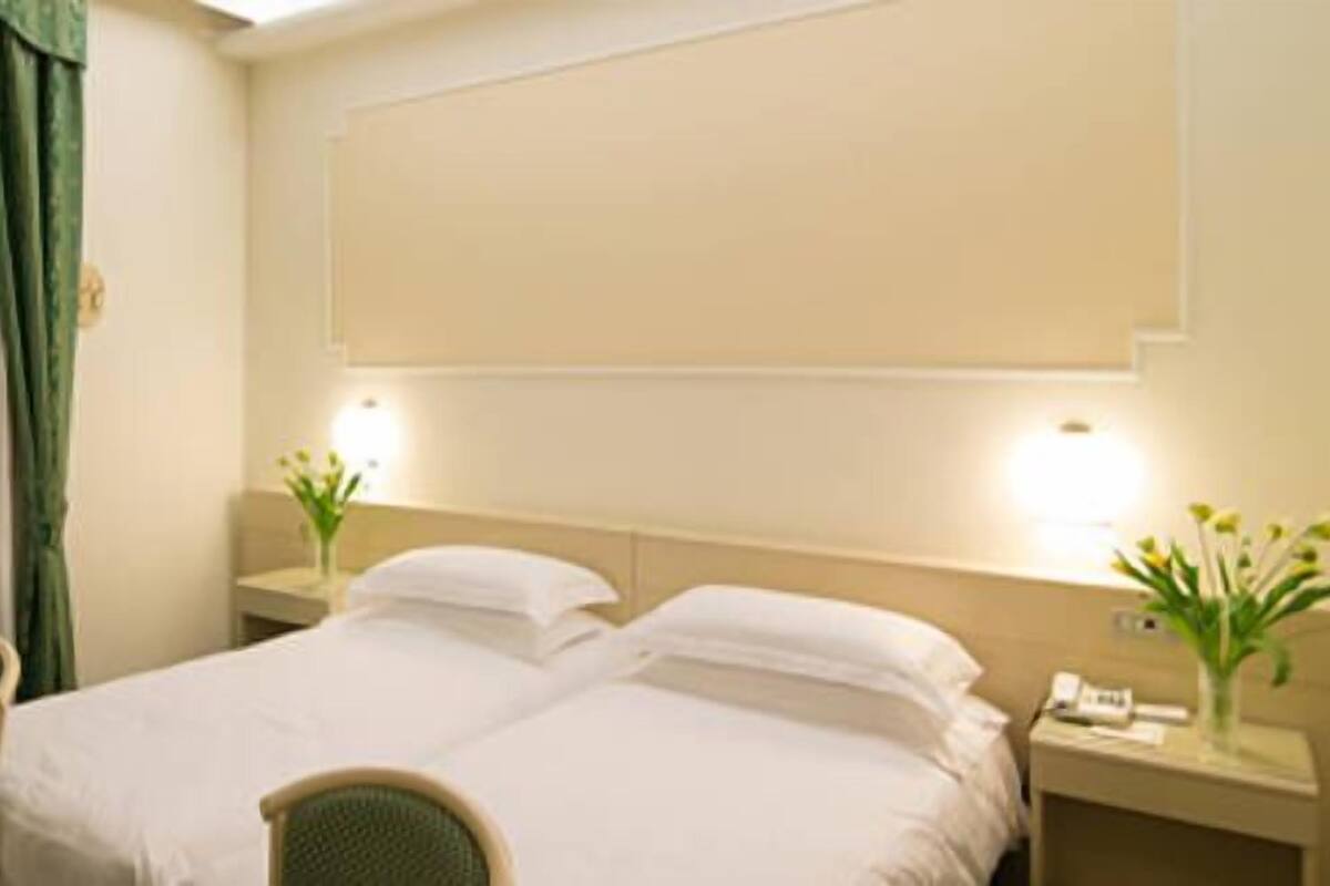 Een hotelkamer met een bed, twee nachtkastjes, een stoel, een raam met gordijnen en een wandlamp.