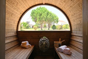 A wooden sauna with a large arched window, a stone shelf, and towels on benches. - Quinta d'Anta - Hotel Rural (Figueira da Foz)