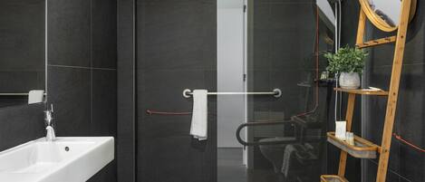 Un baño moderno con un lavamanos blanco, un box de ducha de vidrio, un estante escalonado de madera y un espejo grande.
