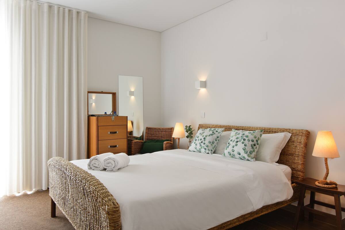 A neatly made bed with a headboard, a wooden dresser, a mirror, and two bedside lamps.