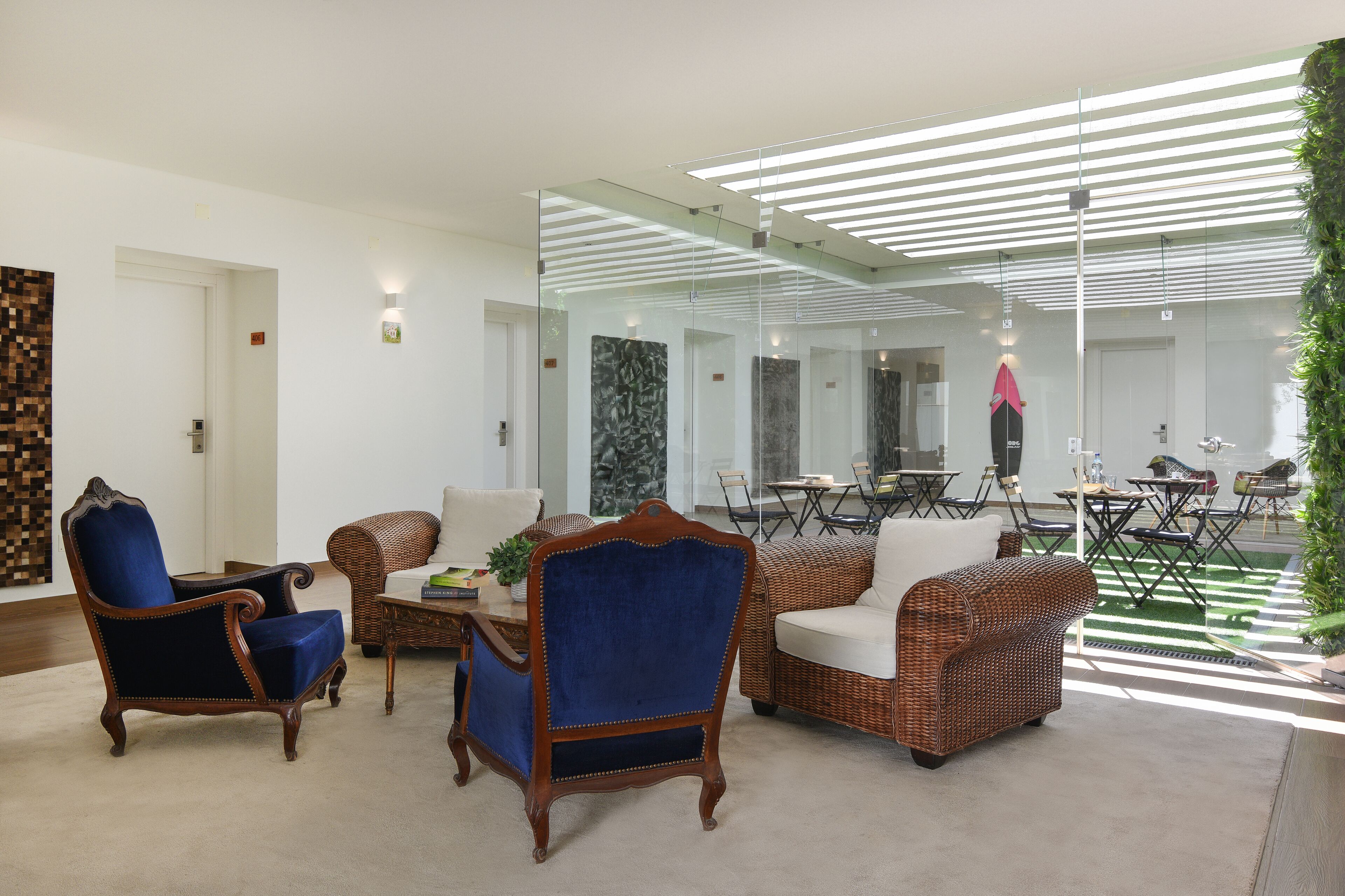 A modern lounge area with a mix of classic and contemporary furniture, including a blue armchair, a wicker sofa, and a dining table with chairs.