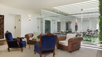 A modern lounge area with a mix of classic and contemporary furniture, including a blue armchair, a wicker sofa, and a dining table with chairs.