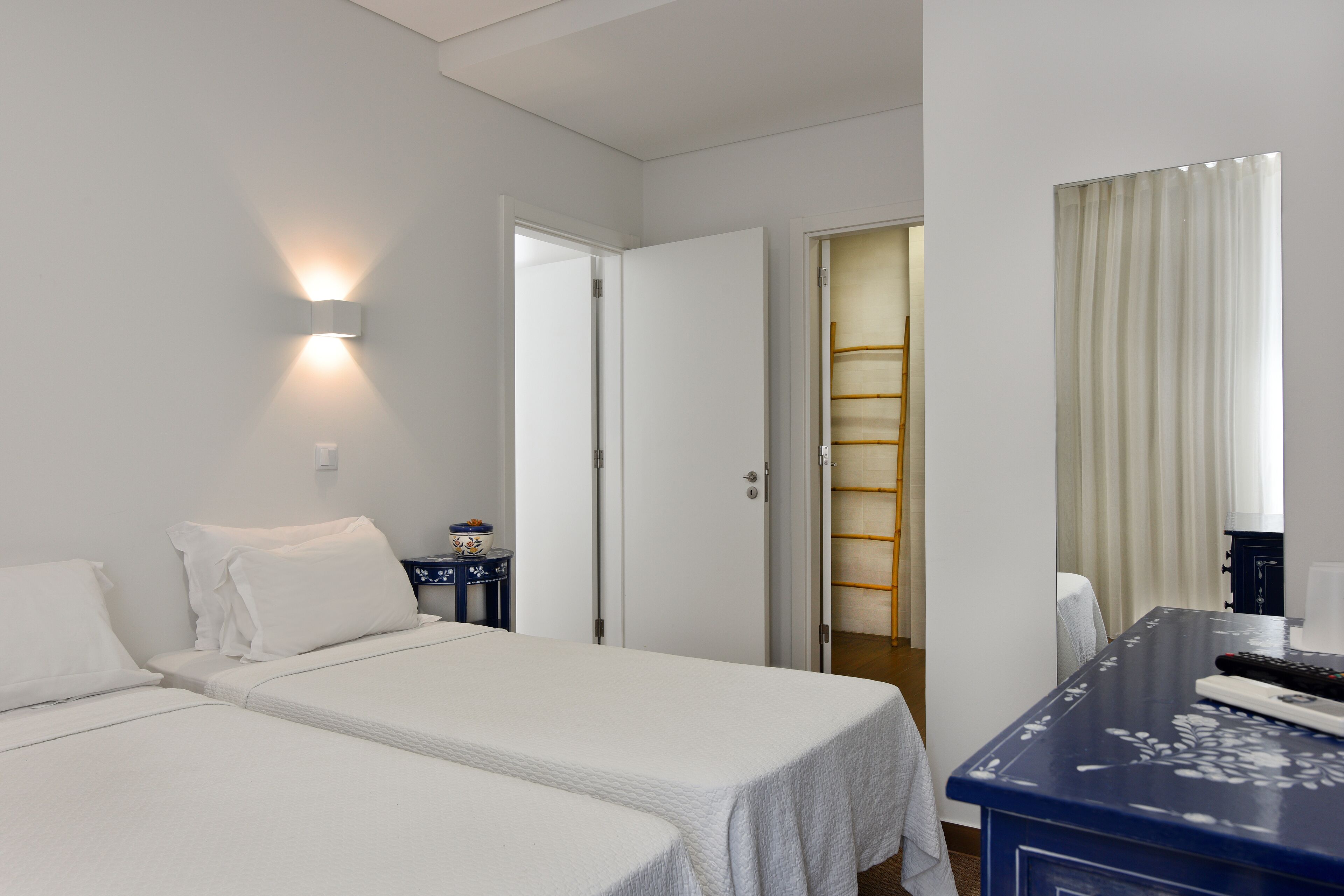 A hotel room with two beds, a desk, a mirror, and a door leading to a bathroom.