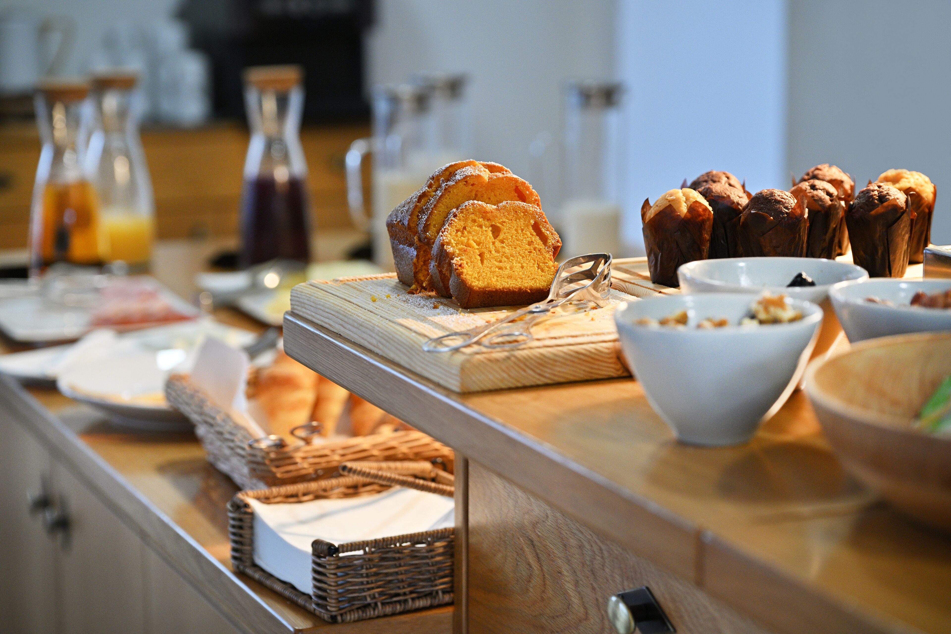 Ein Frühstücksbuffet mit verschiedenen Backwaren, darunter Brot und Muffins, sowie mehreren Schüsseln mit Speisen.