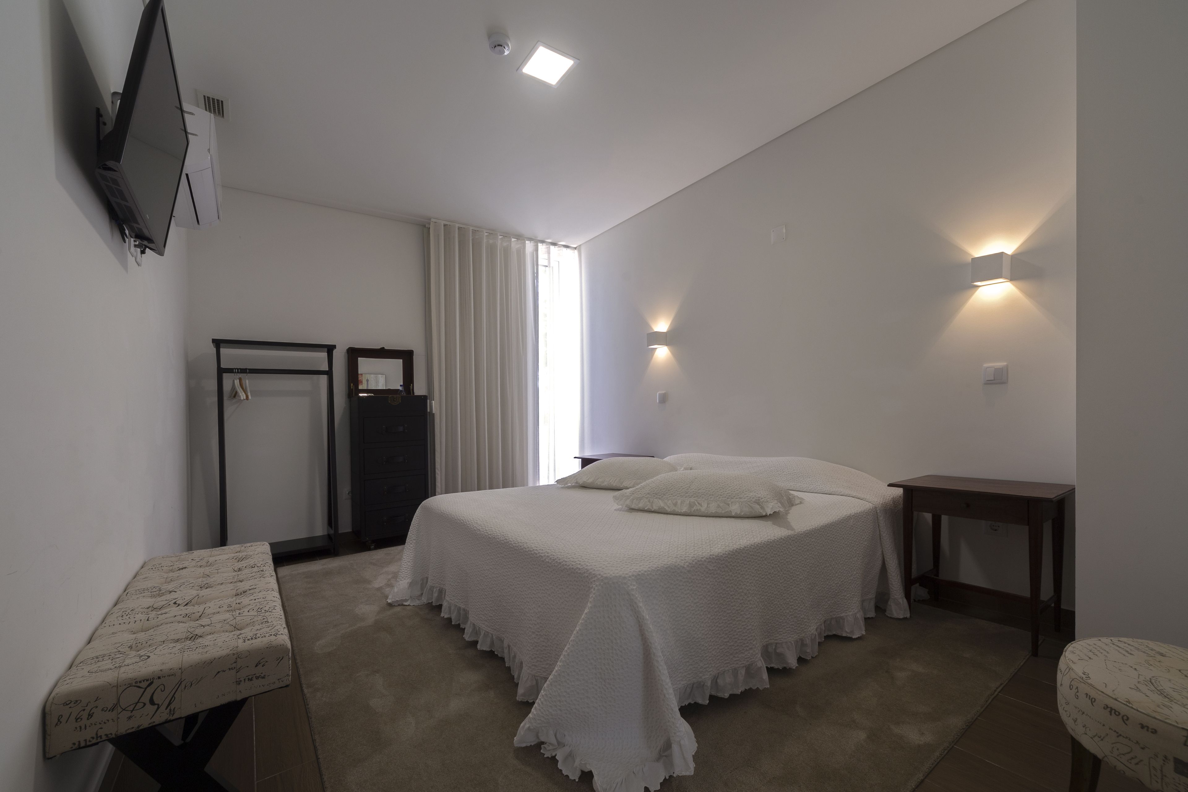 A bedroom with a bed, a bedside table, a wardrobe, a mirror, and a TV mounted on the wall.