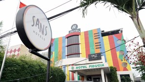 A hotel with a colorful facade, multiple signs including 'SANS HOTELS' and 'HOTEL FIDUCIÀ', and a parked car in front.