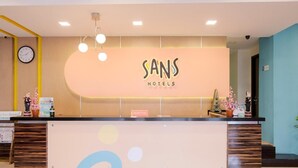 A hotel reception desk with a modern design, a clock on the wall, and a sign indicating the reception area.