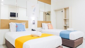 A hotel room with two beds, a mirror, a wardrobe, and a small shelf.