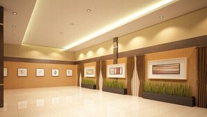 A spacious, well-lit lobby with a tiled floor, framed artwork on the walls, and a large window with curtains.